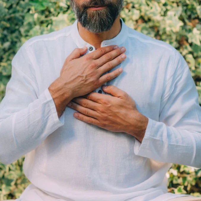 A man sitting cross-legged outdoors with his hands on his heart