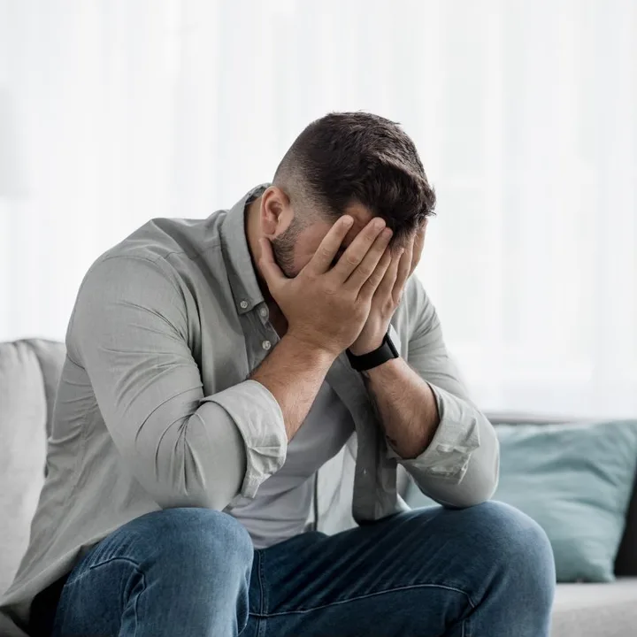 A man sitting on a couch with his face in his hands